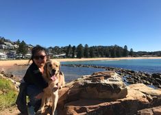 a woman and her dog sitting on rocks by the water