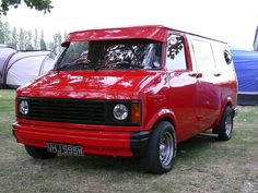 a red van parked on top of a grass covered field