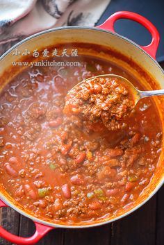 a ladle full of chili and meatballs in a red pot on a wooden table