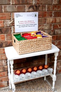 a white table topped with a basket filled with fruit and vegetables next to a brick wall