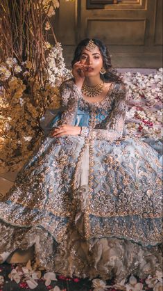 a woman in a blue and gold gown sitting on a bed of flowers with her hands to her face