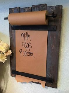 a sign that says milk eggs bacon hanging on a wall next to a vase with flowers