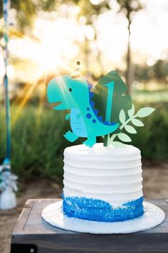 a blue and white cake with a dinosaur topper