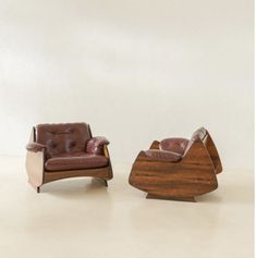 two leather chairs sitting next to each other on top of a floor in front of a white wall