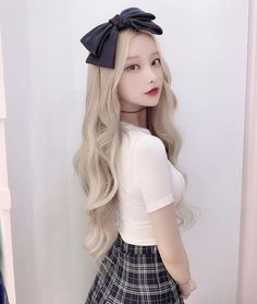 a doll with long blonde hair and a bow on her head is standing in front of a white wall