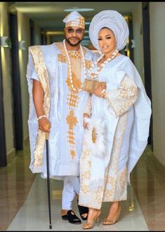 two people dressed in white and gold posing for the camera with one holding a cane