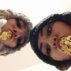 two people with noodles in their mouths are looking up at the camera while wearing hats