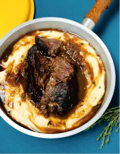 a bowl filled with mashed potatoes and meat on top of a blue tablecloth