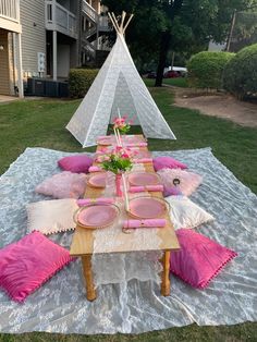 a table set up with pink plates and napkins for a birthday party in front of a teepee tent