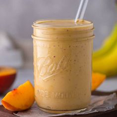 a mason jar filled with peach smoothie on top of a wooden cutting board next to sliced oranges and bananas