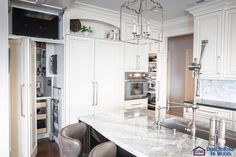 a kitchen with white cabinets and marble counter tops, two chairs in front of the island