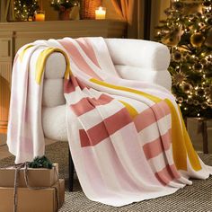 a white chair with a pink and yellow striped blanket on it next to a christmas tree