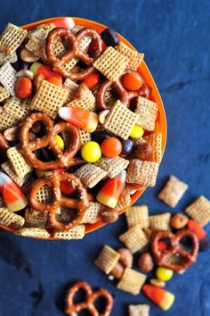 a bowl full of halloween snack mix with pretzels and candy corn on the side