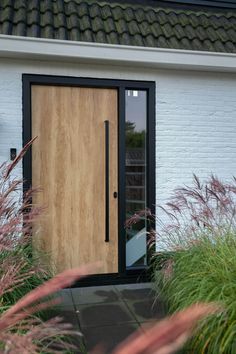 a wooden door sitting in the middle of a lush green garden next to a white brick building