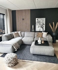 a living room with a large sectional couch and ottoman in the middle, along with black walls