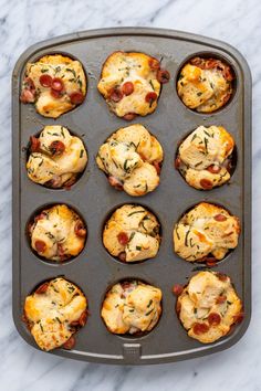 mini pizzas in a muffin tin on a marble countertop, ready to go into the oven