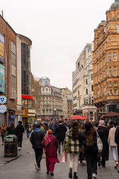 many people are walking down the street in an area with tall buildings and shops on both sides