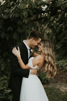 a bride and groom embracing in front of trees