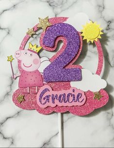 a pink and purple cake topper with a peppo the pig number two on it