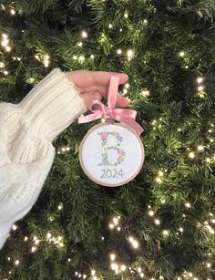 a hand holding a cross stitch ornament in front of a christmas tree with lights