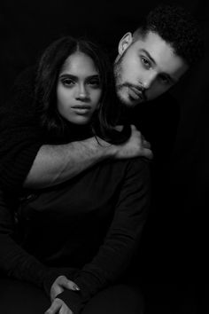 a man and woman sitting next to each other in black and white, posing for the camera