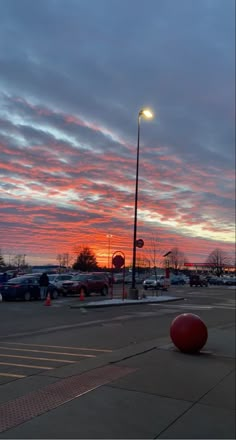 a red ball sitting on the ground in front of a parking lot at sunset or dawn