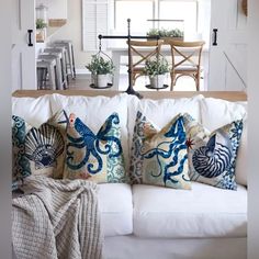 a white couch with pillows on it in front of a window and table behind it