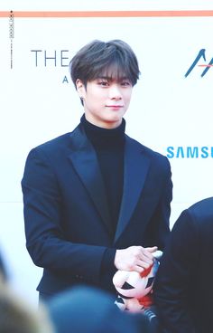 the young man is wearing a black suit and holding his hand in his other hand