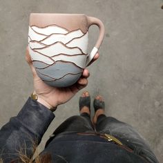 a person holding a coffee cup with mountains on it