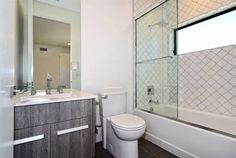 a white toilet sitting next to a bath tub in a bathroom under a window above a sink