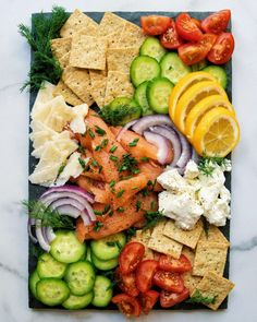 an assortment of vegetables and crackers on a cutting board with lemons, cucumbers, tomatoes, onions, carrots