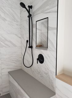 a bathroom with white marble walls and flooring, including a bench that is next to the shower head