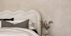 a white bed topped with pillows next to a night stand and vase filled with flowers