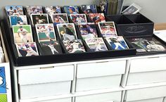 many baseball cards are on top of a white dresser with drawers and bins full of them