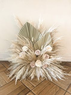 dried flowers and grass on the floor in front of a white wall with wooden floors