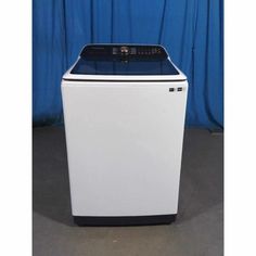 a white and black washer sitting on top of a floor next to a blue curtain