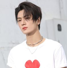 a young man with black hair wearing a white t - shirt and a red heart on his chest