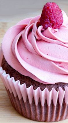 a chocolate cupcake with pink frosting and a strawberry on top, sitting on a wooden surface