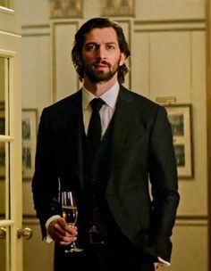 a man in a suit and tie holding a glass of wine standing next to an open door