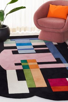 a colorful rug is on the floor next to a pink chair and potted plant