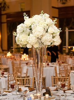 a tall vase filled with white flowers sitting on top of a table covered in gold chairs