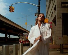 a woman standing on the street in front of a traffic light wearing a white coat