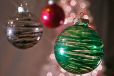 three christmas ornaments hanging from the ceiling in front of a white tree with red and green baubles