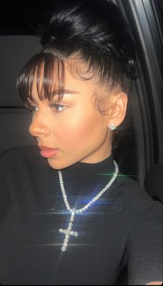 a woman with black hair wearing a cross necklace and pearls on her neck, sitting in a car