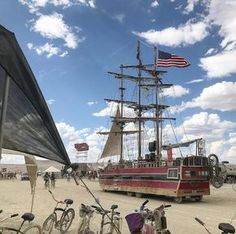 several bicycles are parked in front of a boat on the beach with an american flag flying above it