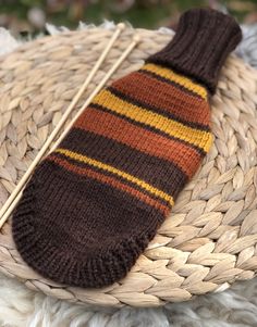 a brown and yellow striped sock sitting on top of a woven basket next to a pair of knitting needles