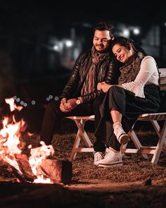 a man and woman sitting on a bench next to a campfire in the night