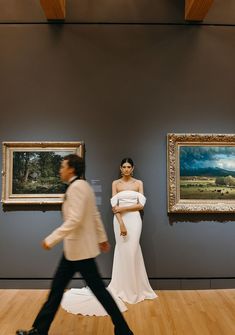 a man and woman walking in front of paintings