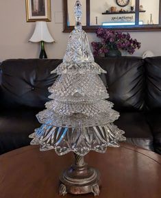 a glass christmas tree sitting on top of a wooden table next to a black couch