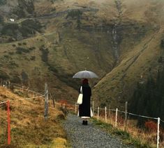 a woman with an umbrella is walking down a path in the mountains near a fence